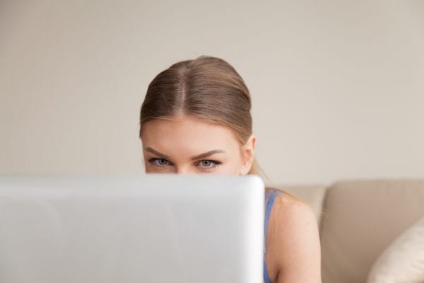 Curious teen using computer, young funny girl peeking over lapto