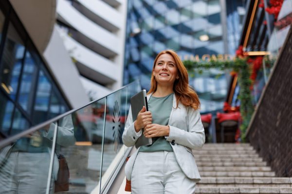 Woman descends stairs with laptop outdoors in business attire